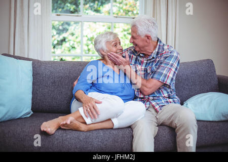Romantico uomo senior toccando moglie guance sul divano Foto Stock