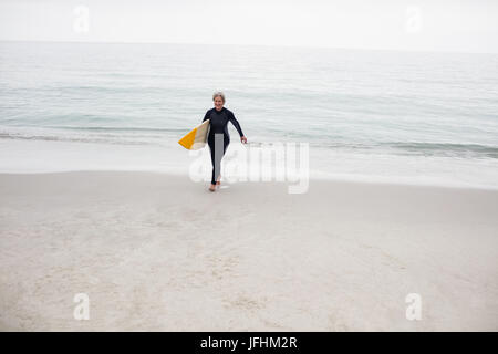 Donna senior di camminare sulla spiaggia con una tavola da surf Foto Stock