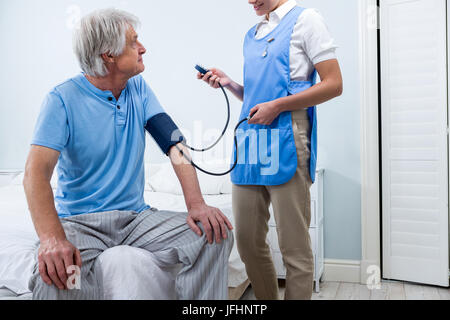 L'infermiera controllando la pressione del sangue di uomo senior a casa Foto Stock