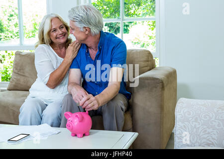 Allegro coppia senior mettendo in moneta di banca piggi a casa Foto Stock