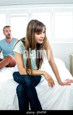 Infastiditi donna seduta sul letto mentre l'uomo grida in background Foto Stock
