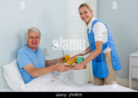 L'infermiera dando la colazione al sorridente uomo senior Foto Stock
