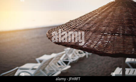 Ombrello in vimini dal sole sulla spiaggia con lettini per prendere il sole e il mare in background Foto Stock