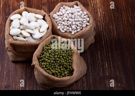 Varietà di Fagioli, diversi tipi di fagioli in sacco di tela su sfondo di legno Foto Stock