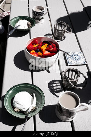 Un bianco tavolo in legno top con una sana colazione su di esso nel mezzo di un vivacemente colorato della frutta con fragole, mirtilli e pesche in Foto Stock