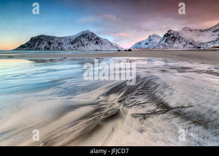 Cielo rosa nel surreale Skagsanden spiaggia circondata da montagne coperte di neve, Isole Lofoten Norvegia del Nord Europa Foto Stock