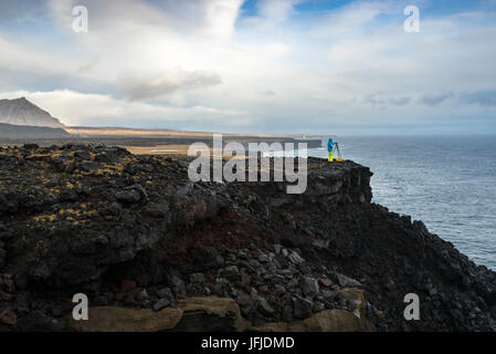 Un fotografo è di scattare le foto con il cavalletto in piedi sulle scogliere vicino Londrangar, Snaefellsjoekull National Park, Western Islanda, Europa Foto Stock