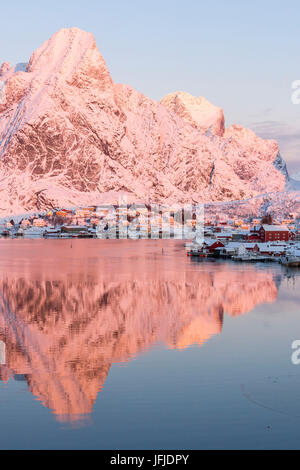 Pink sunrise e cime innevate il telaio il mare ghiacciato e il villaggio di pescatori di Reine Bay Nordland Isole Lofoten in Norvegia Europa Foto Stock