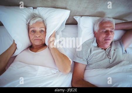 Moglie bloccando le orecchie con cuscino mentre il marito russare sul letto Foto Stock