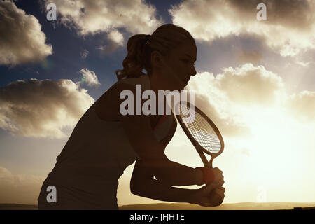 Atleta giocando a tennis con la racchetta contro il cielo nuvoloso Foto Stock