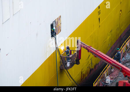 Saldatura del lavoratore una riparazione sul lato di una grande nave in bacino di carenaggio, di essere guardato da tre compagni di lavoro Foto Stock