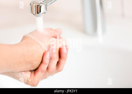 Una donna di lavare le mani sotto acqua corrente dalla gru Foto Stock