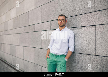Allegro giovane uomo bello in occhiali da sole mantenendo le mani nelle tasche Foto Stock