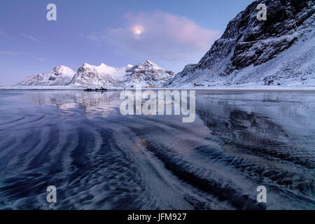 Le onde e il ghiaccio nel surreale Skagsanden spiaggia circondata da vette innevate Flakstad Nordland county Isole Lofoten in Norvegia Europa Foto Stock