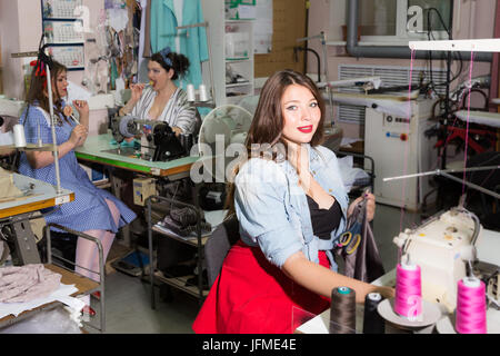 Bella curva modelli femmina immaginato come pinup seamstresses presso un laboratorio di abbigliamento Foto Stock