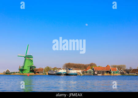 Tipico mulino a vento e barche nel villaggio di pescatori di Zaanse Schans incorniciata dal fiume Zaan Olanda settentrionale dei Paesi Bassi in Europa Foto Stock