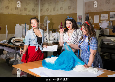 Bella curva modelli femmina immaginato come pinup seamstresses presso un laboratorio di abbigliamento Foto Stock