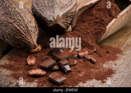 Baccelli di cacao con le fave di cacao, la polvere di cacao e cioccolato di blocco sul tavolo di legno Foto Stock