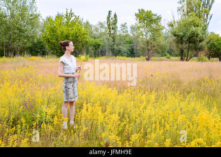 Una donna adulta si alza in un prato ricoperto con il Galium verum fiori, noto anche come lady's bedstraw o bedstraw giallo, con un mazzetto di giallo flowe Foto Stock