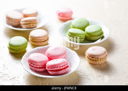 Tre piastre con amaretti rosa, verde e marrone e perle di perla sul tavolo Foto Stock