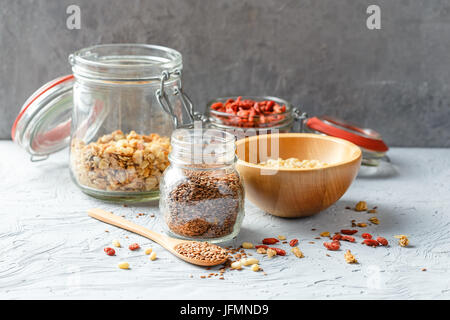 Semi di lino, goji bacche, granola, pinoli in vasetti di vetro su uno sfondo grigio Foto Stock