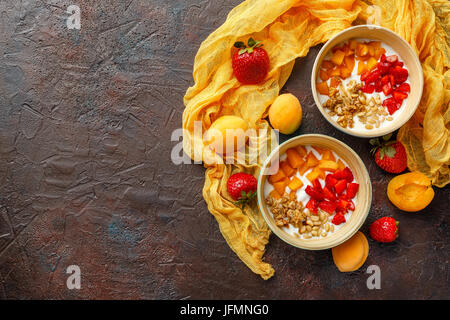 Lo yogurt naturale con pezzi di Albicocche Fragole, granola e pinoli in due ciotole su broun scuro dello sfondo. Vista da sopra con posto per il testo Foto Stock