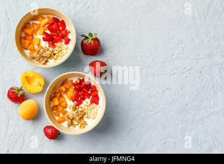 Lo yogurt naturale con pezzi di Albicocche Fragole, granola e pinoli in due ciotole su sfondo chiaro. Vista da sopra con posto per il testo Foto Stock