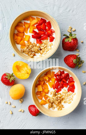 Lo yogurt naturale con pezzi di Albicocche Fragole, granola e pinoli in due ciotole su sfondo chiaro. Vista superiore Foto Stock