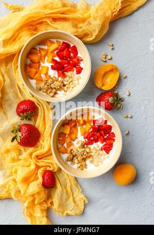 Lo yogurt naturale con pezzi di Albicocche Fragole, granola e pinoli in due ciotole su sfondo chiaro. Vista superiore Foto Stock