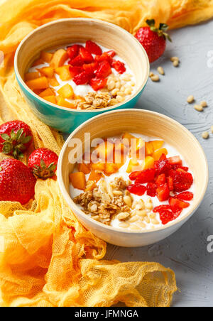 Lo yogurt naturale con pezzi di Albicocche Fragole, granola e pinoli in due ciotole su sfondo chiaro Foto Stock