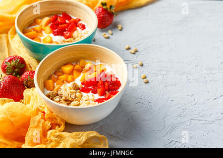 Lo yogurt naturale con pezzi di Albicocche Fragole, granola e pinoli in due ciotole su sfondo chiaro Foto Stock