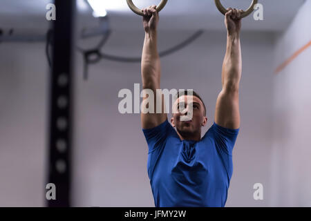 Fitness uomo bello fare immersione esercizio utilizzando anelli in palestra Foto Stock