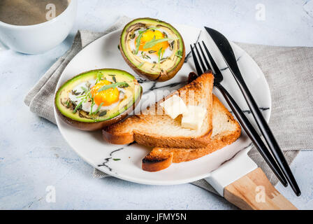 Vegano sana prima colazione. La dieta. Cotta di avocado con uovo e insalata fresca da foglie di rucola, toast e burro. Su un marmo bianco della piastra, un calcestruzzo leggero tabella. Foto Stock