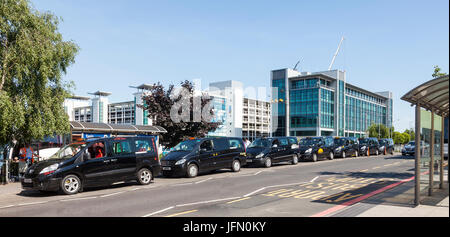 Taxi con taxi schierate in Comet Road, Birmingham Airport, West Midlands, England Regno Unito. Parcheggio multipiano e Diamond House in background. Foto Stock