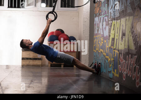 Fitness uomo bello fare immersione esercizio utilizzando anelli in palestra Foto Stock