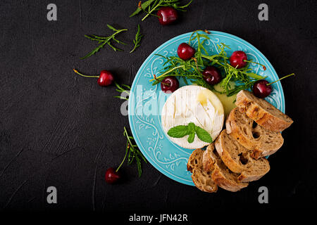 Cotta formaggio Camembert, toast e insalata di rucola con ciliegie dolci. Lay piatto. Vista superiore Foto Stock