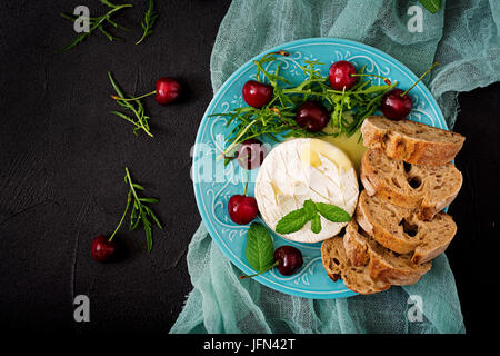 Cotta formaggio Camembert, toast e insalata di rucola con ciliegie dolci. Lay piatto. Vista superiore Foto Stock