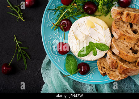 Cotta formaggio Camembert, toast e insalata di rucola con ciliegie dolci. Lay piatto. Vista superiore Foto Stock