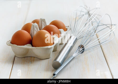 Scatola marrone con uova e fruste per la mantecazione. Foto Stock