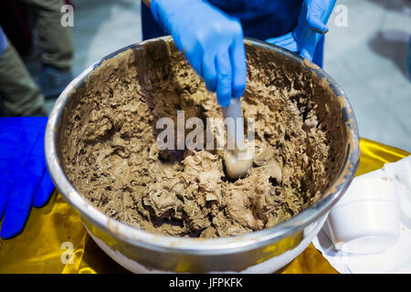 Fatta in Casa il gelato al cioccolato in una ciotola di metallo. Mano umana con guanto blu miscelazione della miscela di dolci. Estremamente gustoso e deliziosi dessert. Caramelle ful Foto Stock