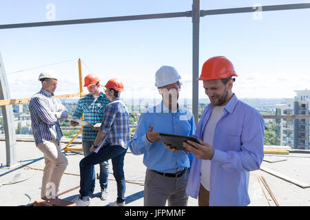 Costruttori sul sito azienda Computer tablet di discutere il progetto di costruzione su team di apprendisti parlando Foto Stock