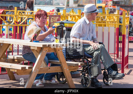 Uomo in una sedia a rotelle con una donna nel parco divertimenti in Dymchurch, Kent, Inghilterra, Regno Unito. Foto Stock