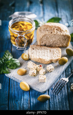 Il formaggio Feta cubo con spezie e semi di oliva sul blu sullo sfondo di legno Foto Stock