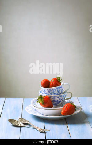 Fragole in coppa vintage e piattini con cucchiai di zucchero sul tavolo rustico Foto Stock