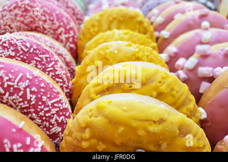 Stuzzicanti multi-colore ciambelle smaltate in righe per la vendita in un negozio di pasticceria in close-up. Foto Stock