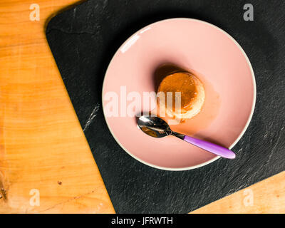 Il budino al flan o crema di caramello è un dessert alla crema con uno strato di caramello morbido sulla parte superiore, le origini sono francesi e spagnole con cucchiaio sopra il tavolo di legno Foto Stock