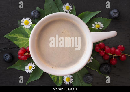 Mattina caffè con margherite, foglie, ribes rosso e mirtilli neri su sfondo di legno. Vista superiore Foto Stock