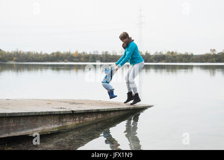 Madre e figlio jumping mano nella mano su una fase di atterraggio in un lago in autunno Foto Stock