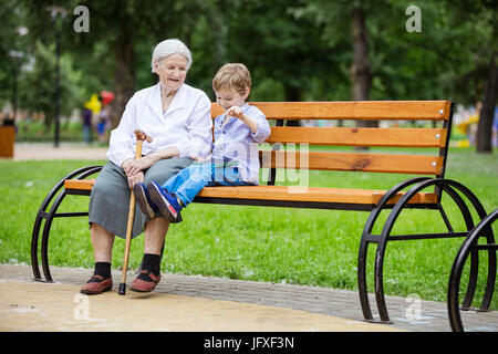 Ragazzo giovane e la sua grande nonna utilizzando tablet mentre è seduto su un banco di lavoro in posizione di parcheggio Foto Stock