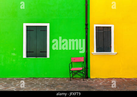 Due finestre con persiane e la parete esterna della casa dipinta in vividi colori verde e giallo a Burano, Italia. Foto Stock